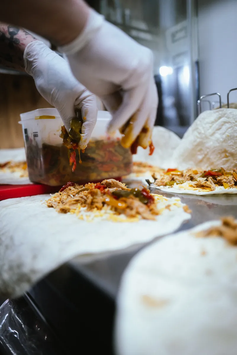 Hände belegen Tortillas mit Pulled Pork und Gemüse